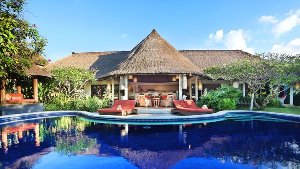 A swimming pool with lounge chairs, a thatched-roof building, and lush greenery.