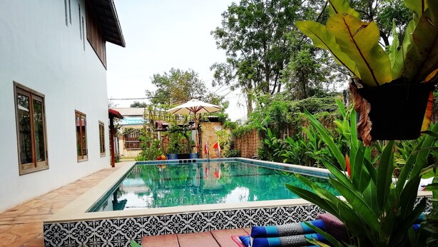 A swimming pool with a tiled edge, surrounded by a garden with various plants and a wooden deck.