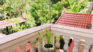 A balcony with a potted plant, a red tiled roof, and a view of greenery.