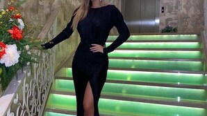 Une femme vêtue d’une robe noire se tient sur un escalier dont les marches sont illuminées en vert. On aperçoit en arrière-plan un mur de pierre et un ascenseur.