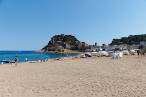 A beach with boats, a castle-like structure, and a clear blue sky.