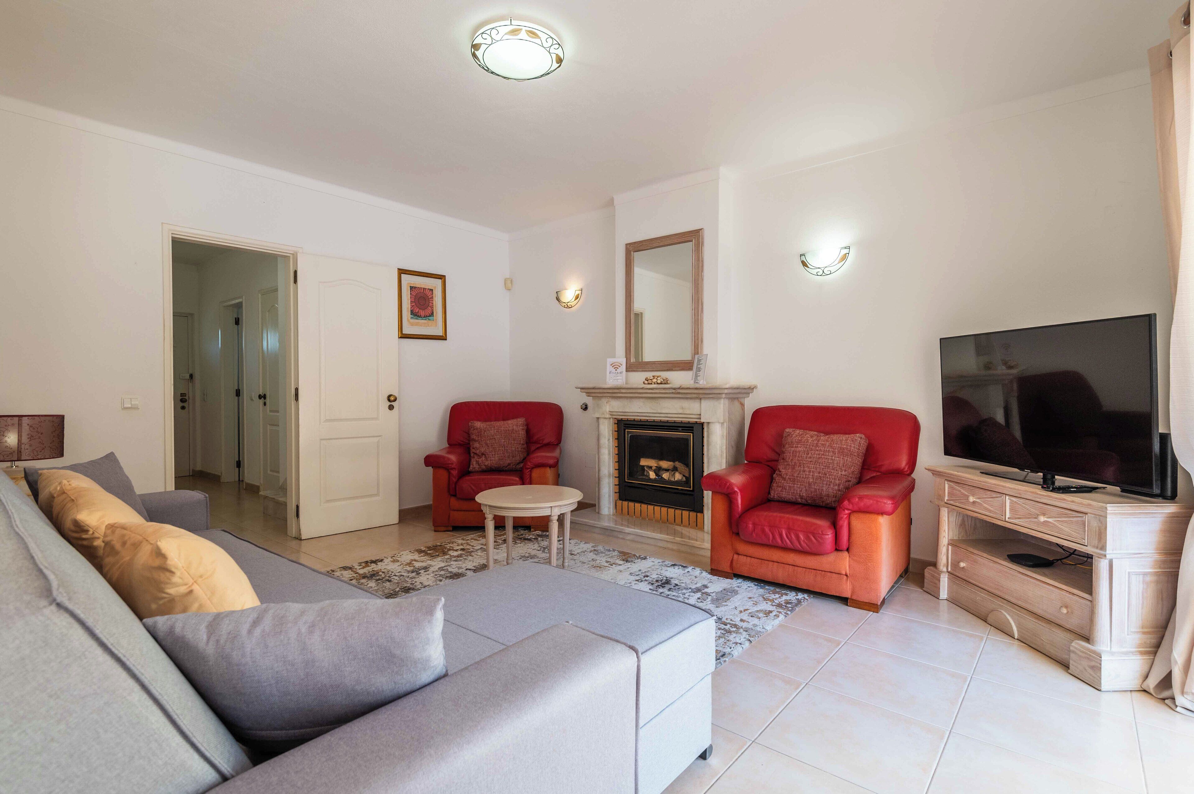A living room with a sofa, two red armchairs, a TV, and a fireplace.