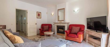 A living room with a sofa, two red armchairs, a TV, and a fireplace.
