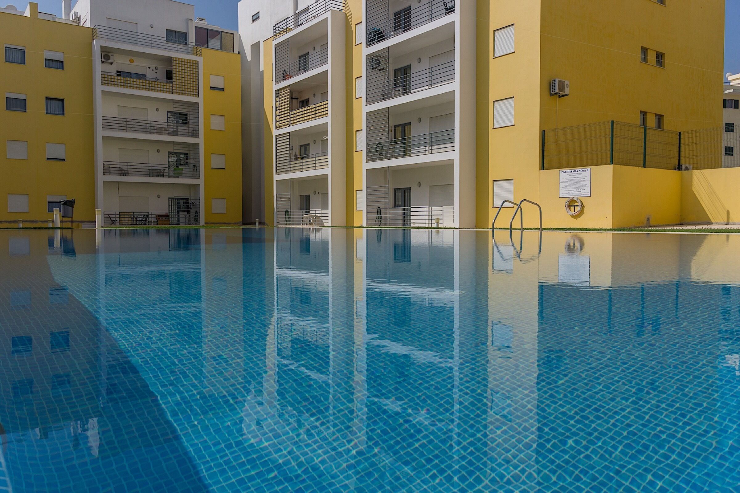 Une piscine à l’eau d’un bleu limpide, entourée de bâtiments jaunes dotés de balcons et de fenêtres.