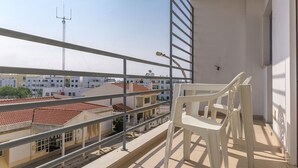 Un balcone con vista su una zona residenziale, dotato di ringhiera, una sedia e una lampada.
