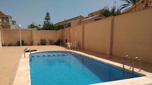 A rectangular swimming pool with a tiled deck, surrounded by a low wall and a few potted plants. - Beautiful apartment in Torrevieja (Torrevieja)