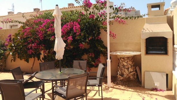 An outdoor patio with a round glass table, metal chairs, a white umbrella, and a brick oven. - Beautiful apartment in Torrevieja (Torrevieja)