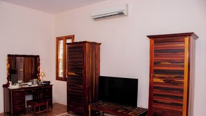 Una sala de estar con televisor, muebles de madera, alfombra estampada y aire acondicionado.
