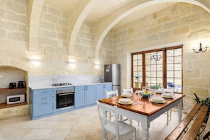A kitchen with blue cabinets, a wooden dining table, white chairs, and a stone wall. - Dar tal-Patri Villa in Gozo with private pool, quiet location & family friendly (L-Għasri)