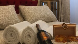 Una cama bien hecha con toallas blancas enrolladas, una botella de vino y una caja de pasteles.