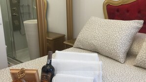 Habitación de hotel con cama, mesita de noche de madera, botella de vino y una caja de pasteles.