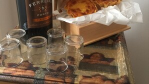 Una botella de vino, una caja de madera con pasteles, y copas para chupitos sobre una mesa.