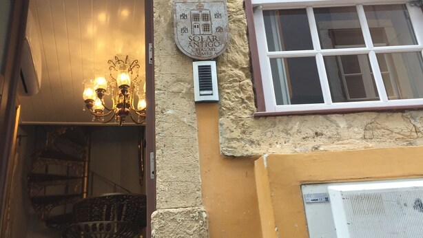 Fachada de piedra de un edificio, una ventana con cortinas rojas y un cartel que dice "SOLAR ANTIGO CHARME COIMBRA".