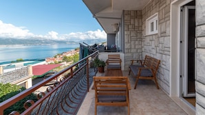Un balcon avec vue sur une étendue d’eau et des montagnes lointaines. On y trouve deux chaises en bois et une petite table.