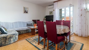 Un salon comprenant un canapé, une table à manger avec des chaises, un téléviseur et une fenêtre avec des rideaux.