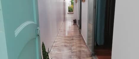 Um corredor com piso de azulejos, um vaso de planta e uma porta à esquerda.