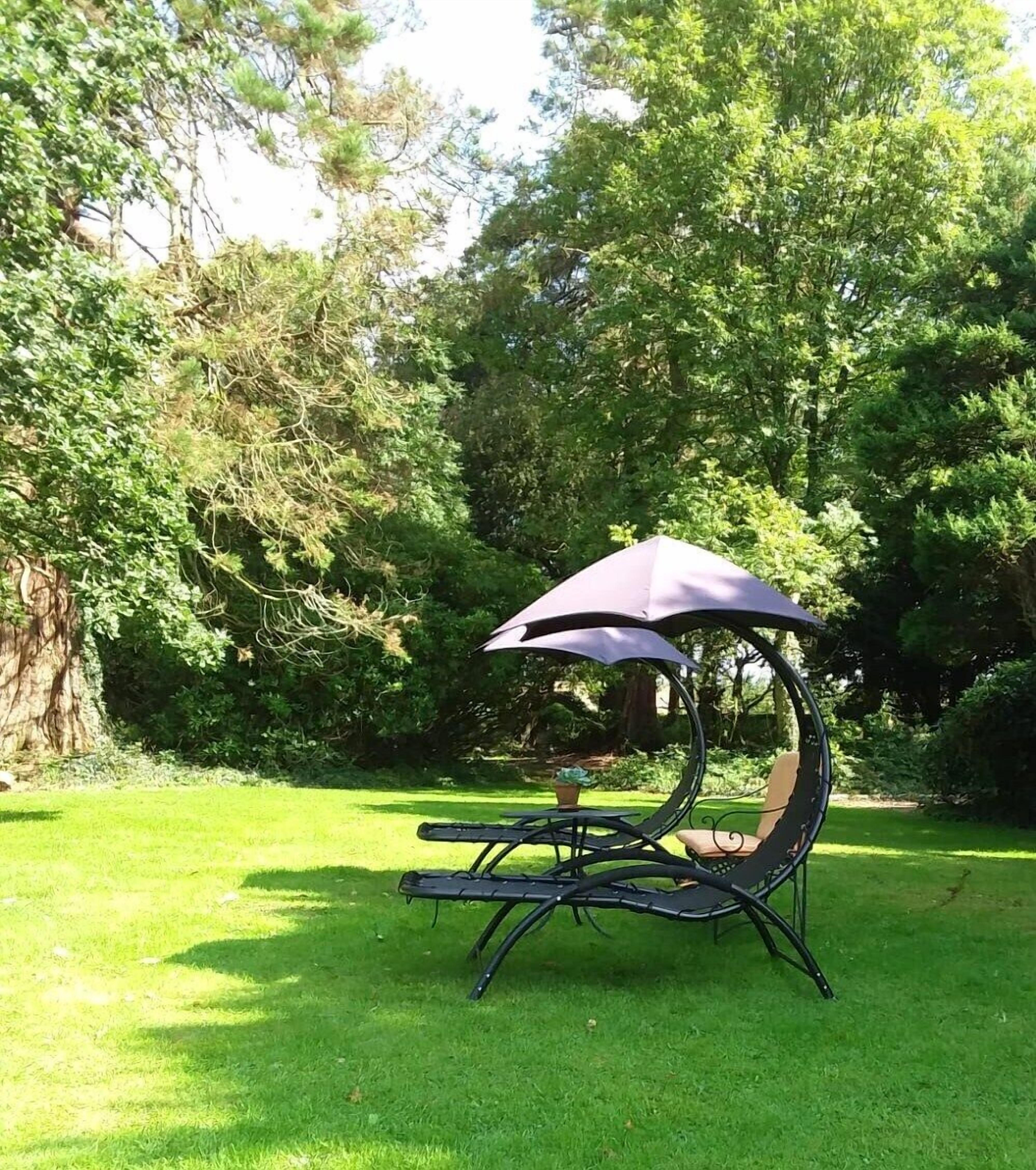 Un jardin avec une balançoire en métal suspendue sous une tonnelle.