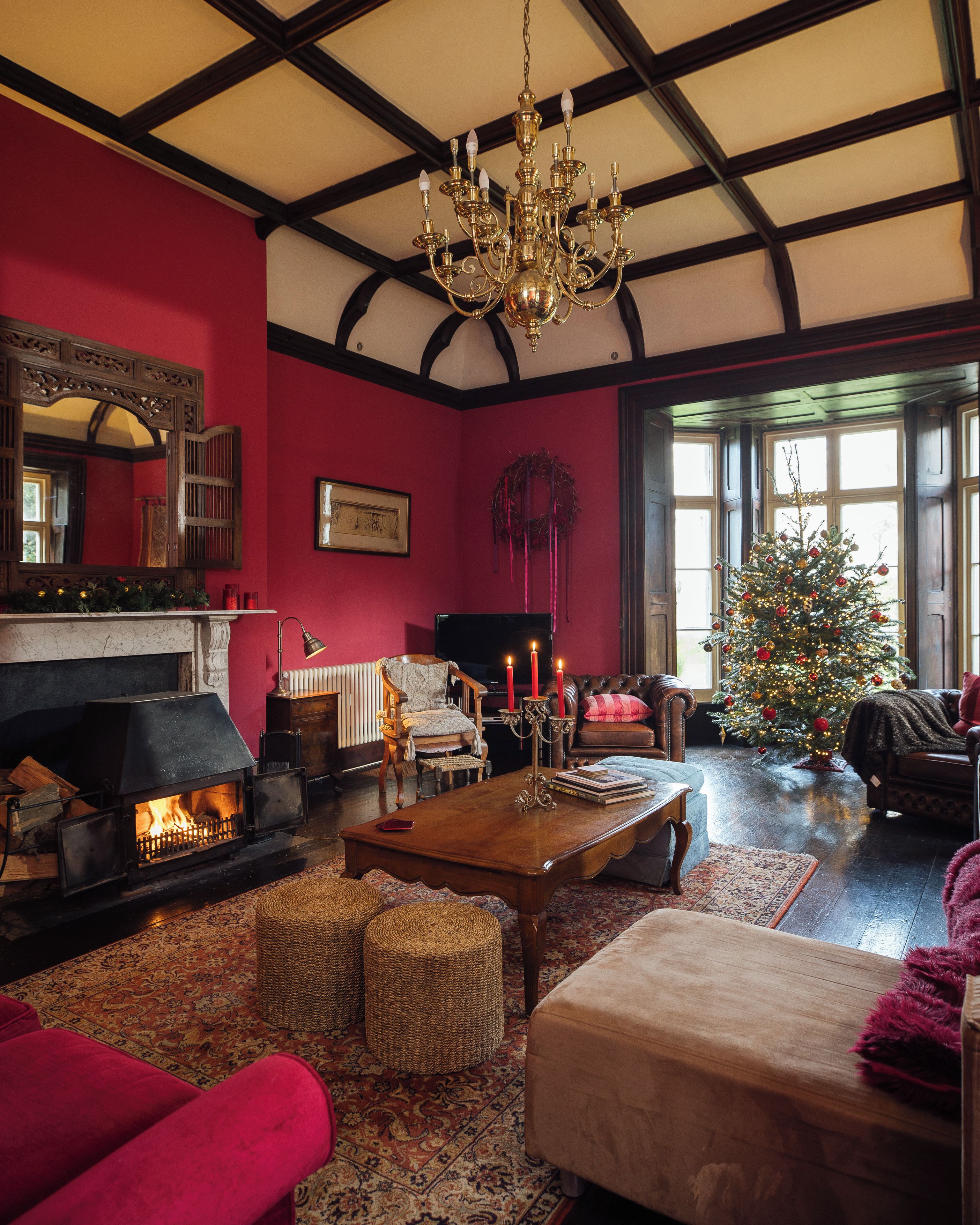 A cozy living room with a fireplace, a Christmas tree, and a large chandelier.