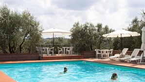 Une piscine où se trouvent deux personnes, entourée de chaises longues blanches et de parasols.