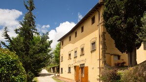 Un bâtiment jaune avec une façade en pierre, des portes en bois et un chemin de gravier menant à l’entrée.