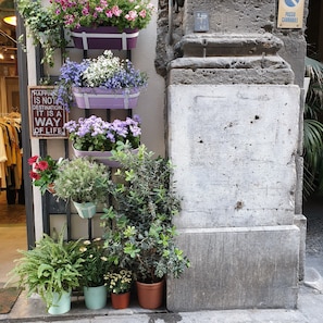A storefront with multiple flower planters on display, a sign with a quote, and a stone pillar.