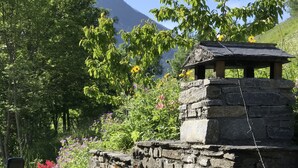 A stone structure with a chimney, surrounded by lush greenery and flowers. - Les Arcs skiing: Charming chalet in an idyllic location minutes from chair lift (Villaroger)