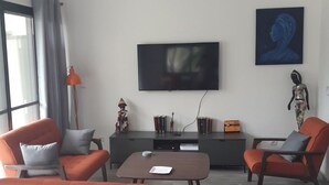 Un salon moderne avec des canapés orange, un téléviseur à écran plat, un ventilateur de plafond et un tableau accroché au mur.