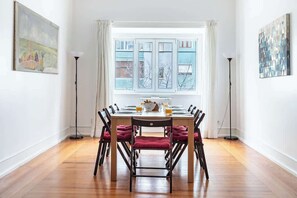 A dining area with a table set for six, chairs with red cushions, a window with curtains, and artwork on the walls.
