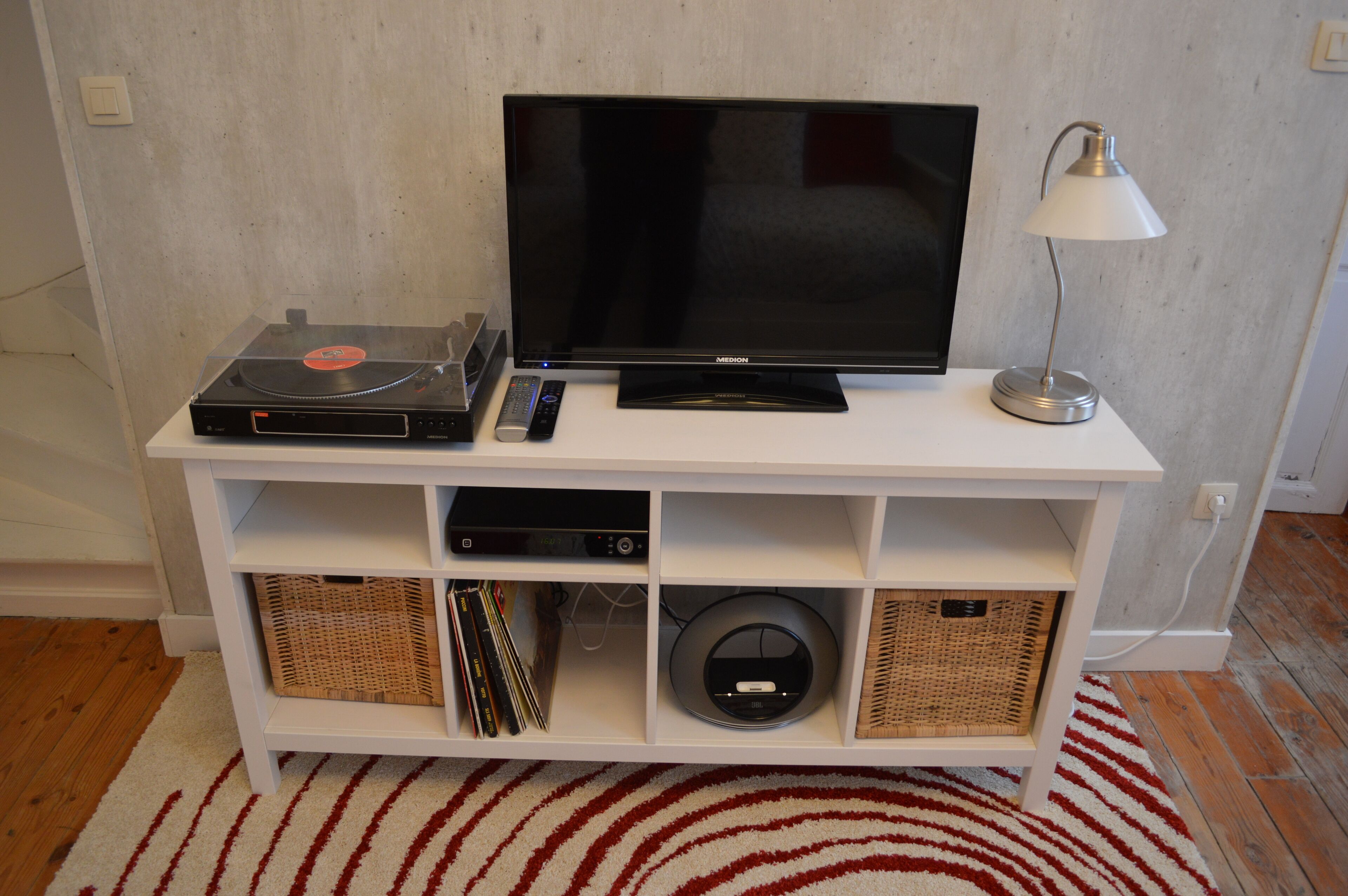 A white entertainment unit with a flat-screen TV, a turntable, and a lamp.