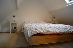 A bedroom with a wooden bed, a white nightstand, a small shelf, a desk, and a skylight.