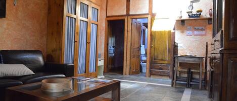 Una sala de estar con un sofá de cuero, una mesa de centro de madera y una zona de cocina con armarios de madera y piso de baldosas.