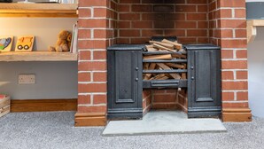 Una chimenea con repisa de piedra, rodeada de paredes de ladrillo rojo, y un estante de madera con libros y juguetes.