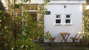 Un jardín con mesa y dos sillas de madera, un muro de piedra y un cartel que dice 'The Old Church House'.