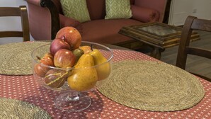 A dining table with a fruit bowl, a woven placemat, and a patterned tablecloth.