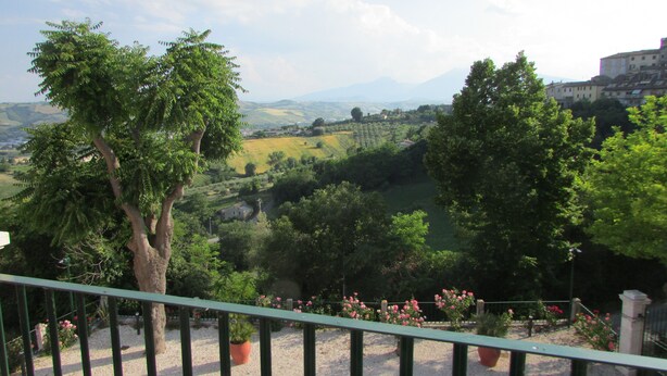 A balcony with a view of a green landscape, trees, and distant buildings.