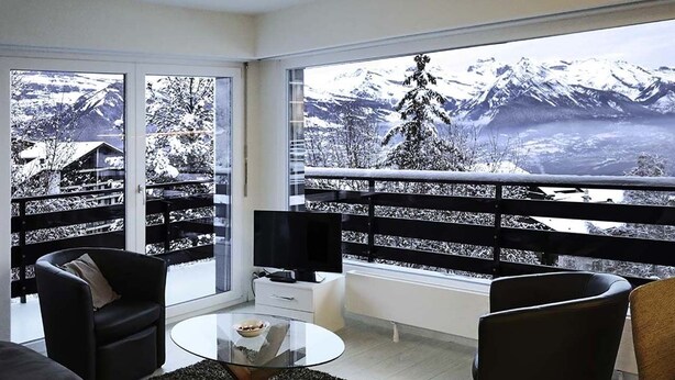 A modern living room with a glass coffee table, black and brown sofas, and a large window offering a view of snow-covered mountains. - PRETTY APARTMENT 4 to 6 people (Nendaz)