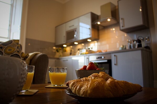 En frukostuppläggning med en croissant, apelsinjuice och jordgubbar på ett bord.