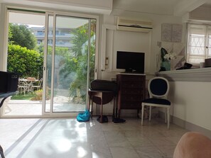 Un salon doté d’une porte-fenêtre coulissante donnant sur une terrasse, d’un téléviseur à écran plat, d’un meuble en bois et d’un fauteuil.