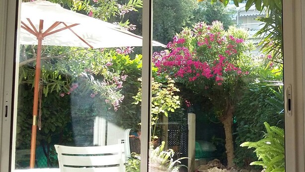 A sliding glass door leading to a garden with a white chair, a small table, and a pergola with pink flowers. - Residential area 5 minutes from the beach  (Cannes)