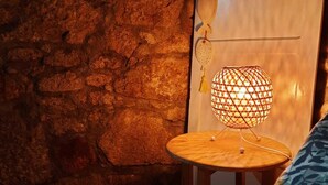A room with a stone wall, a wooden table with a hanging lamp, and a patterned sofa.