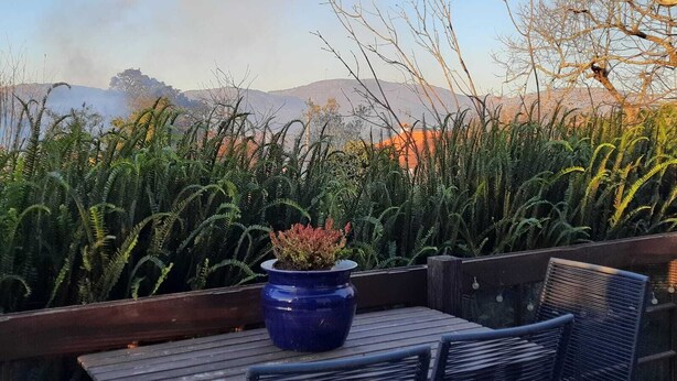 A wooden deck with a table and chairs, a blue pot with a plant, and a view of mountains and a cityscape in the background.
