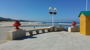 A beachside promenade with a concrete pathway, red urns, and a yellow building.
