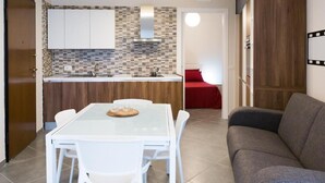 Une cuisine moderne avec des meubles blancs, un pare-feu en carrelage et un coin repas comprenant une table en verre et des chaises blanches.