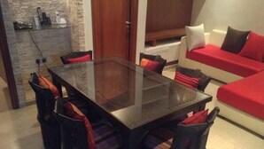Ein Essbereich mit einem Tisch mit Glasplatte, umgeben von Stühlen, einem roten Sofa und einer Steinwand.