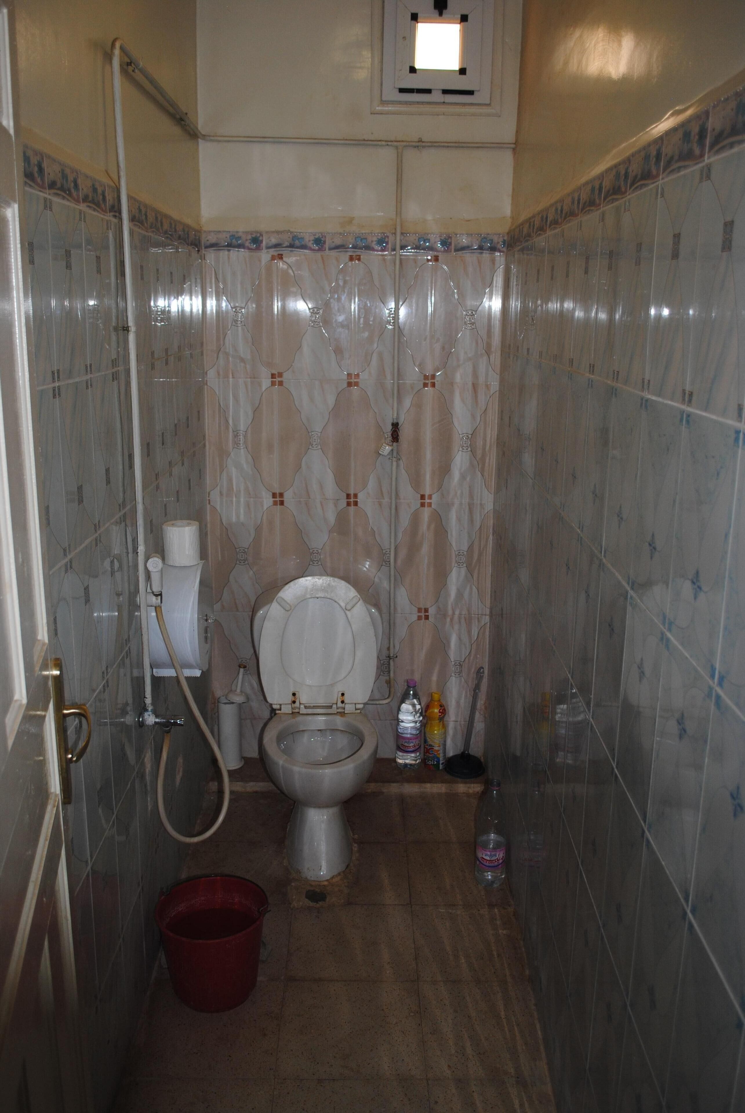 A bathroom with a toilet, a shower, and a red bucket on the floor.