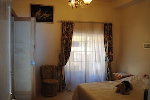 A bedroom with a bed, a chair, a small table, and a dog.