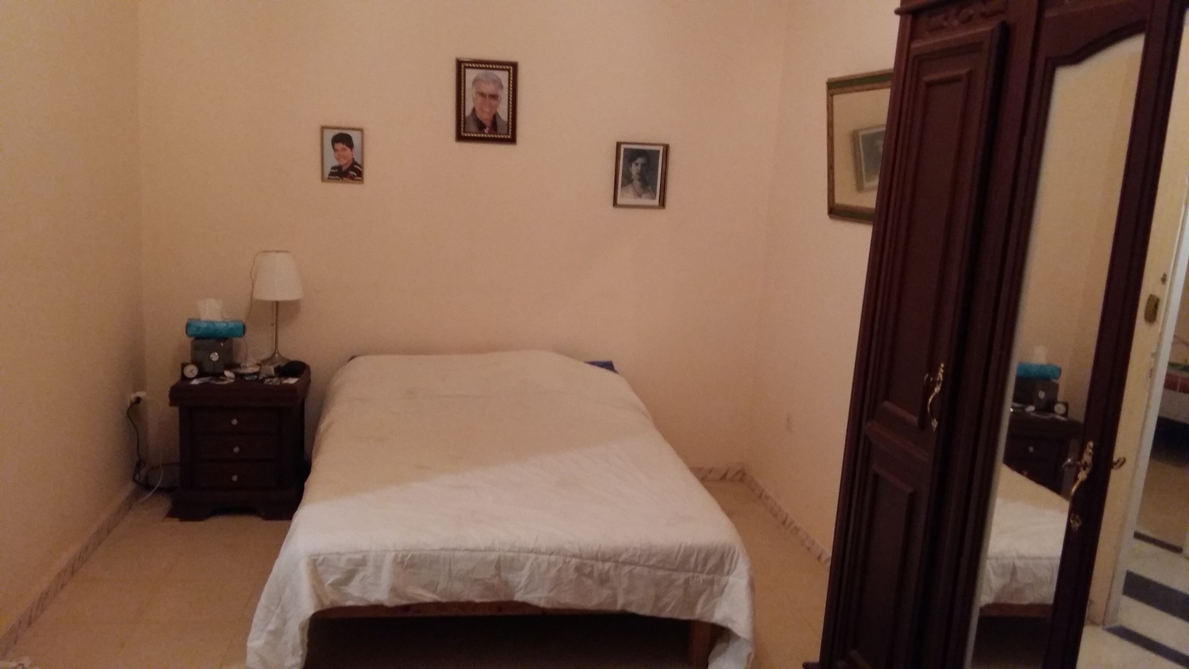 Une chambre avec un lit simple, une table de chevet avec une lampe et une porte en bois.