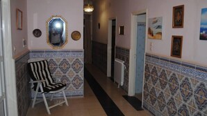 A hallway with patterned tile walls, a chair, a mirror, and artwork.