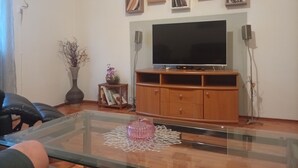 Sala de estar com televisão de tela plana, armários de madeira e mesa de centro de vidro.
