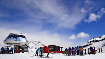 Un centro de esquí con una gran montaña cubierta de nieve al fondo, un telesilla y un edificio con techo rojo.